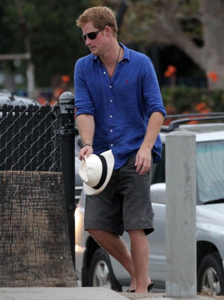 Prince Harry wears shorts with a blue button down shirt and white hat